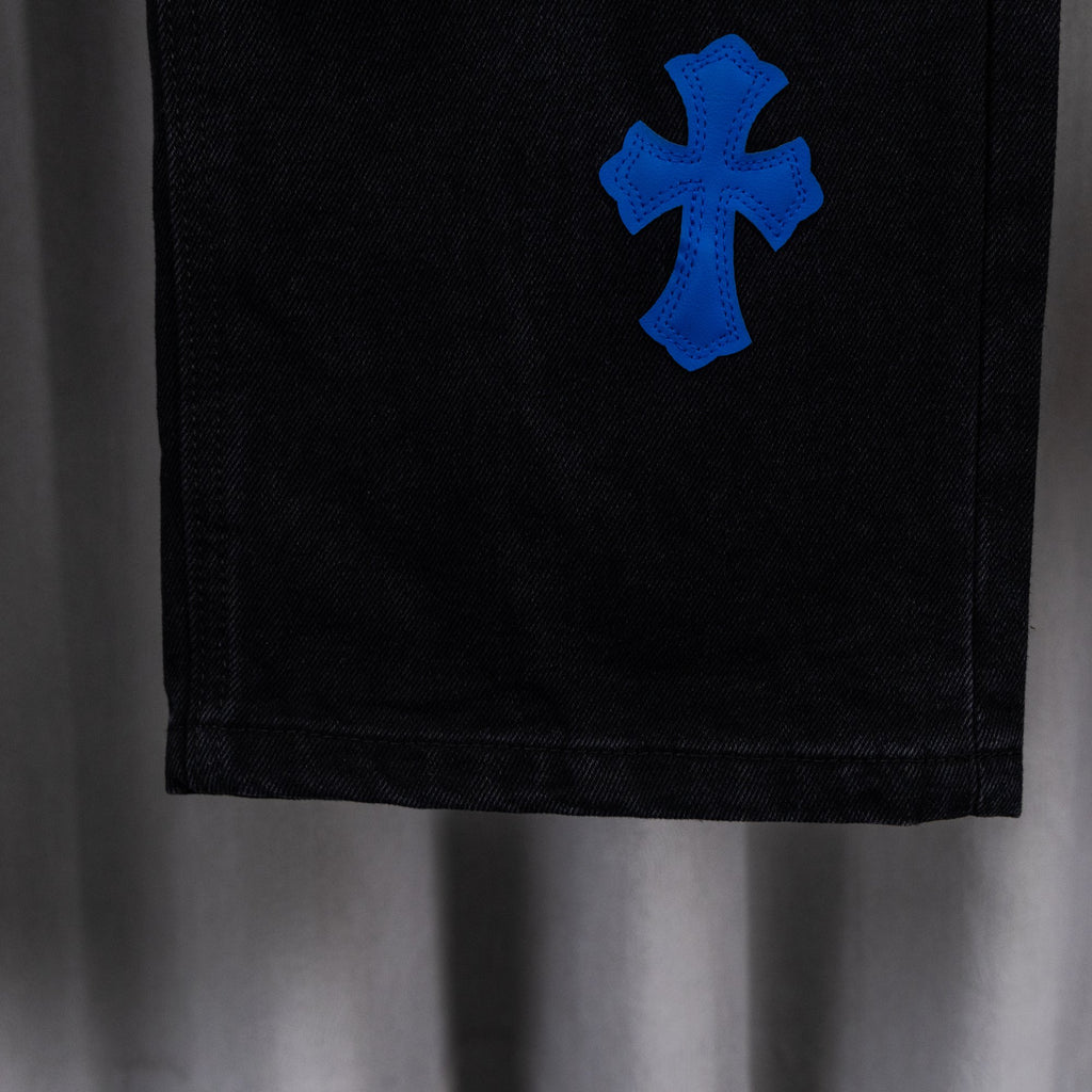 Black denim pant leg with blue cross applique, cropped close-up view.