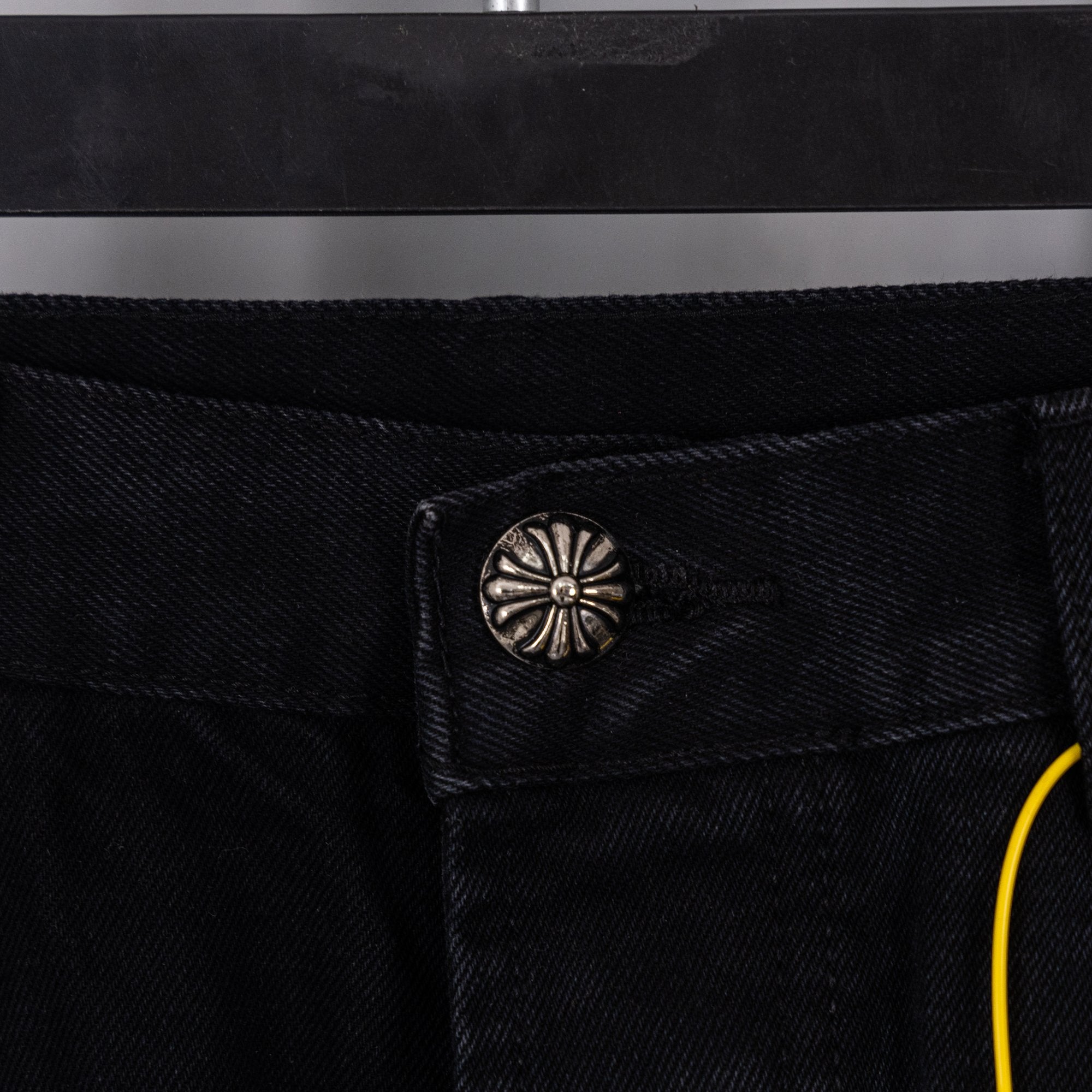 Black denim pants with snap coin pocket and belt loop, close-up detail.