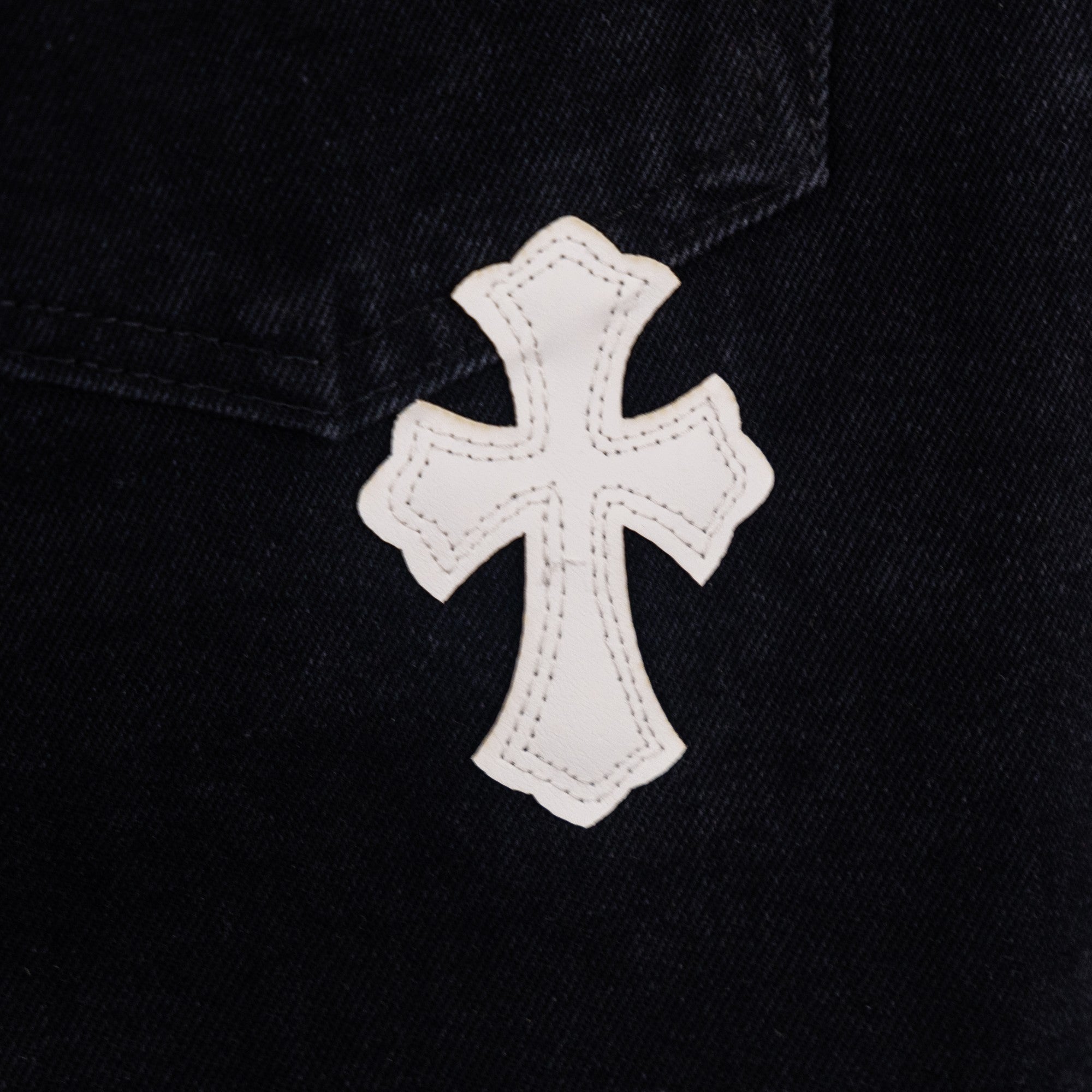 Black denim pants with white cross applique patch on pocket