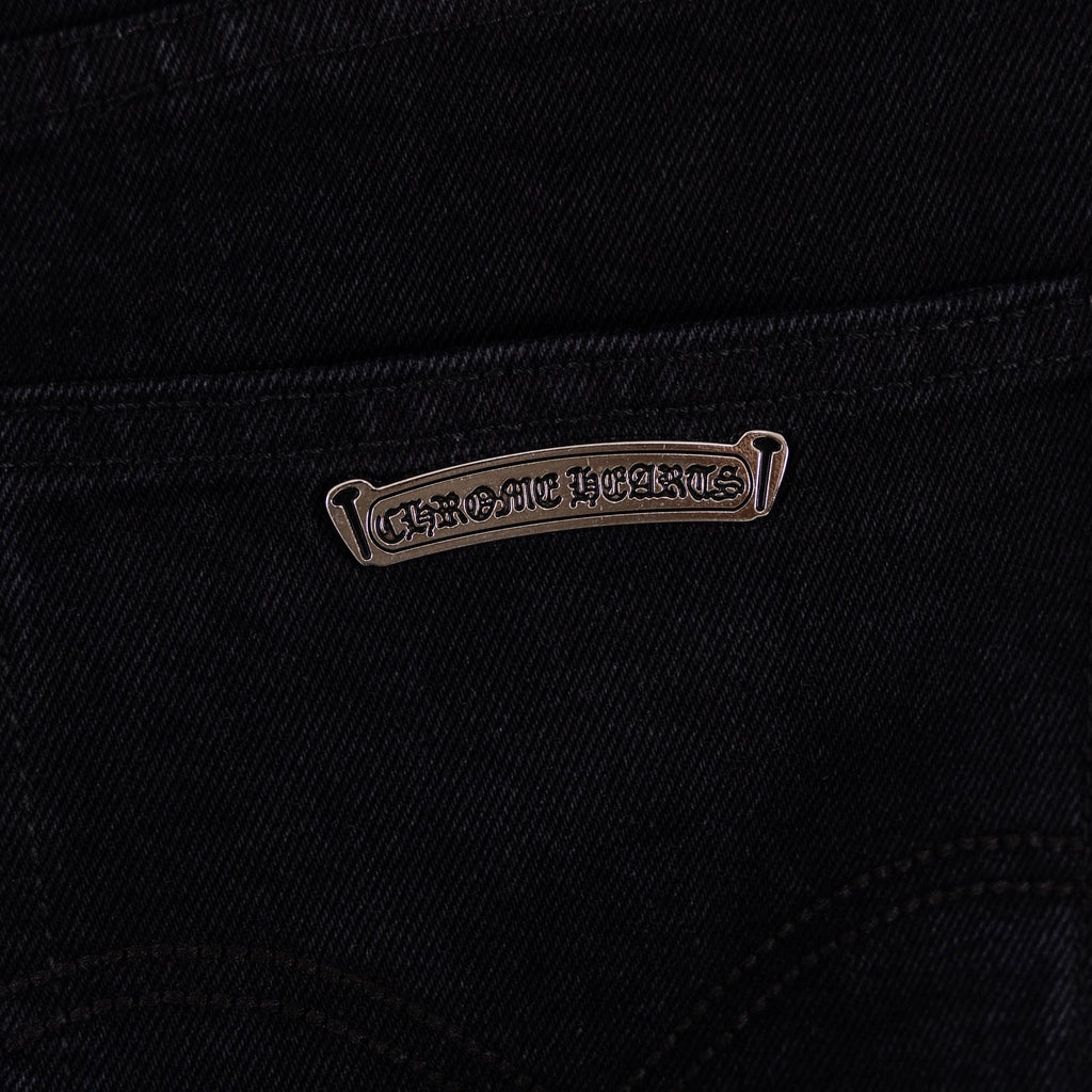 Black denim pants with metal-look logo tag near pocket seam