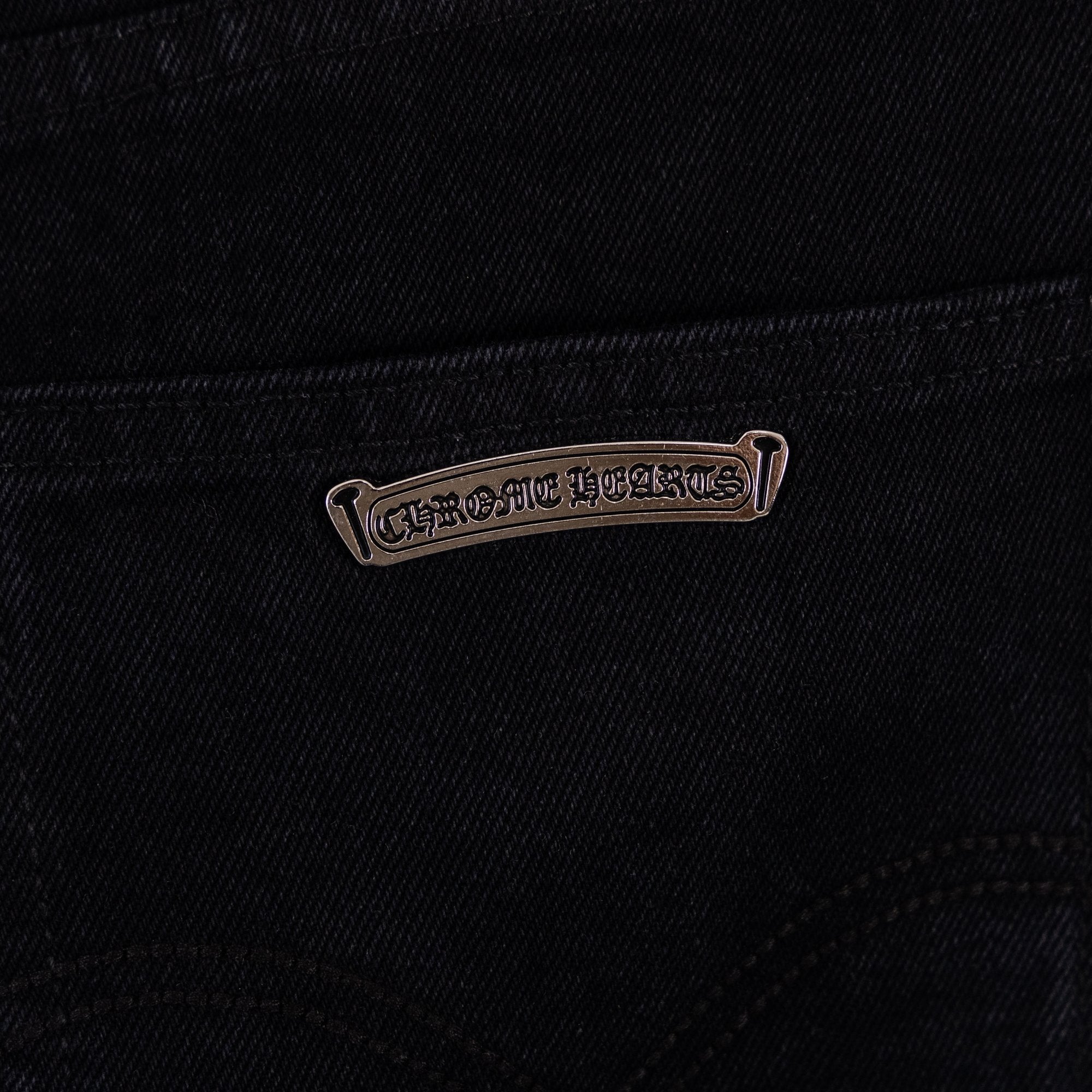 Black denim pants with metal-look logo tag near pocket seam