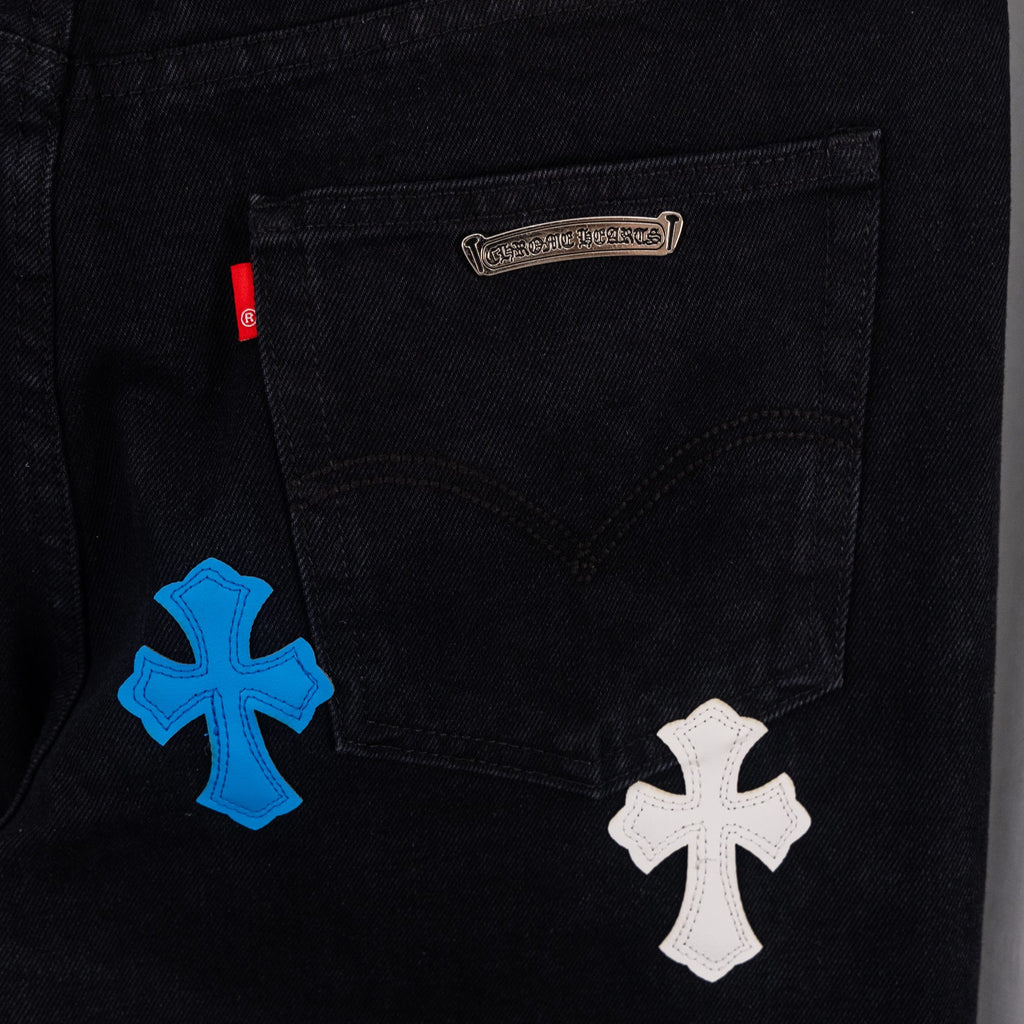 Black denim pants with embroidered cross patches on the front pockets