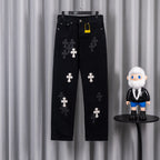 Black pants with embroidered white cross patches, front view on hanger