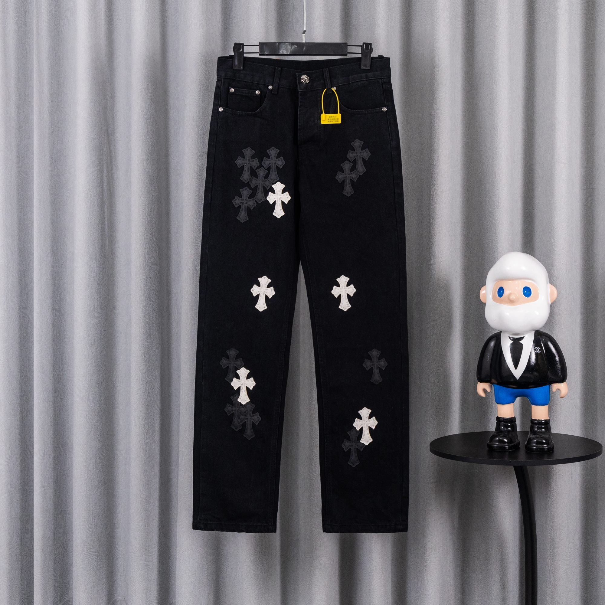 Black pants with embroidered white cross patches, front view on hanger
