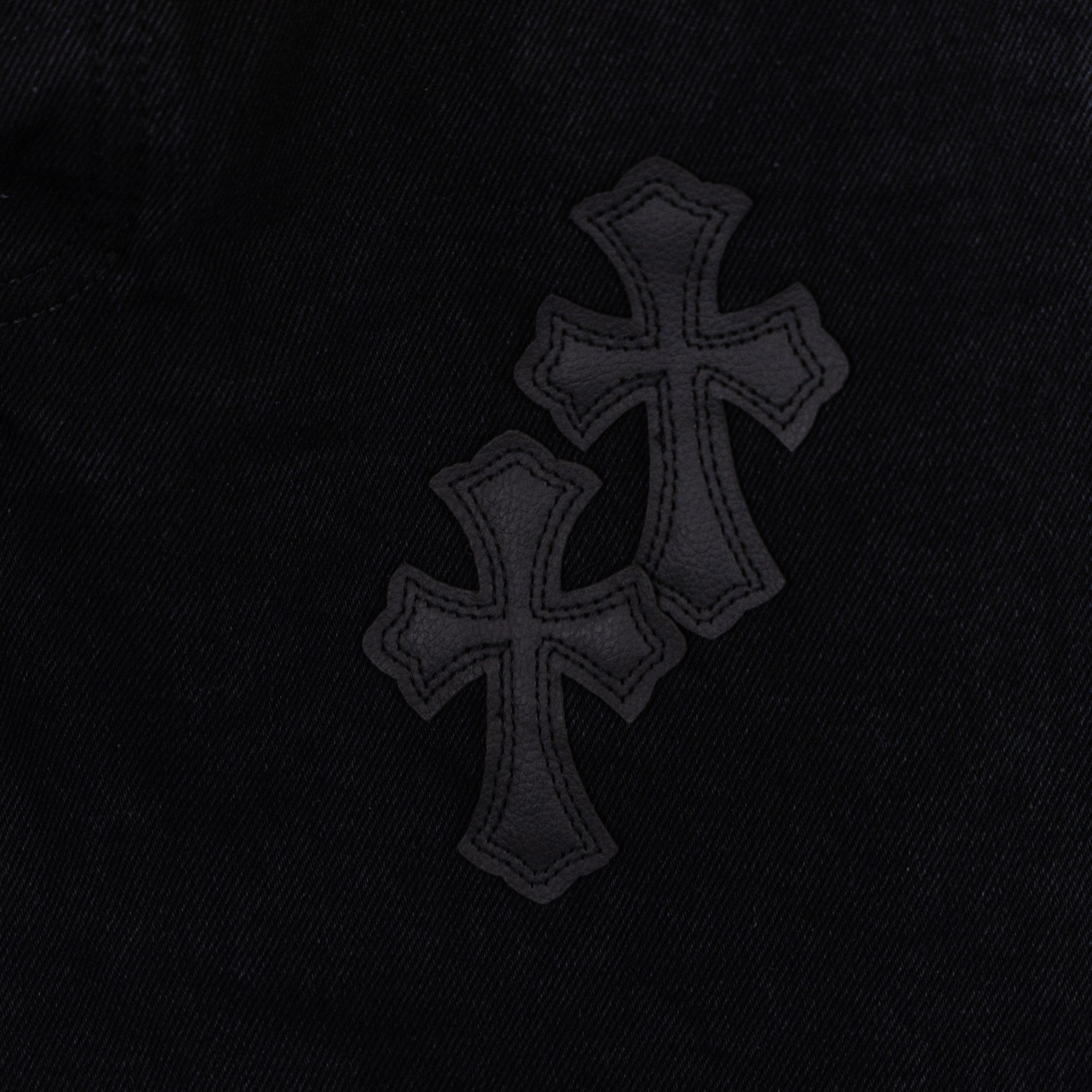 Black denim pants with dark cross patches along the leg