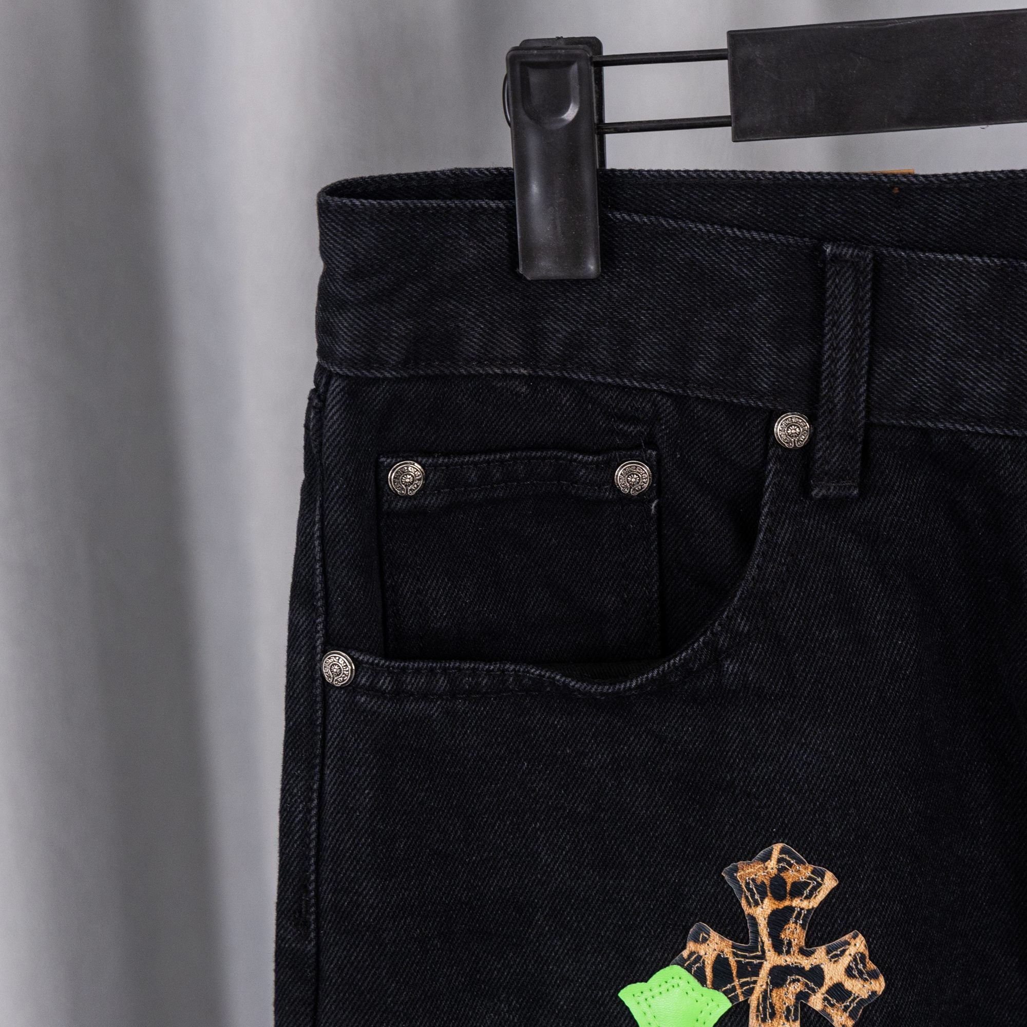 Black denim pants with front pockets and green cross embroidery on leg