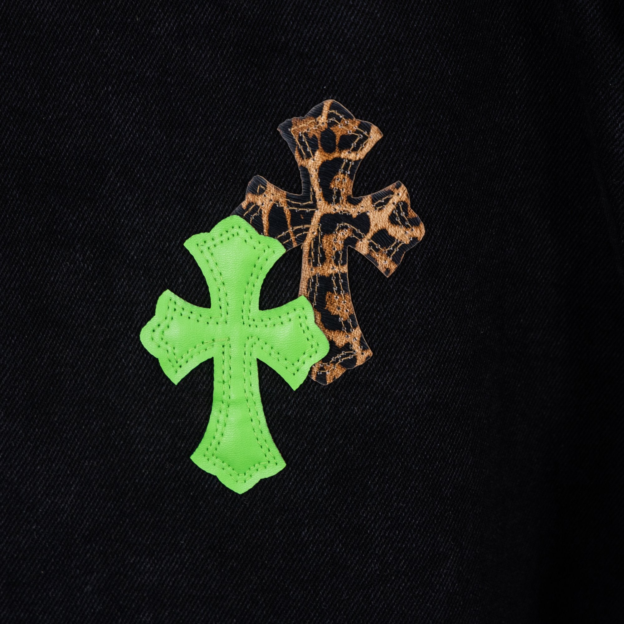 Black denim pants close-up of green cross embroidery with tan cross overlay