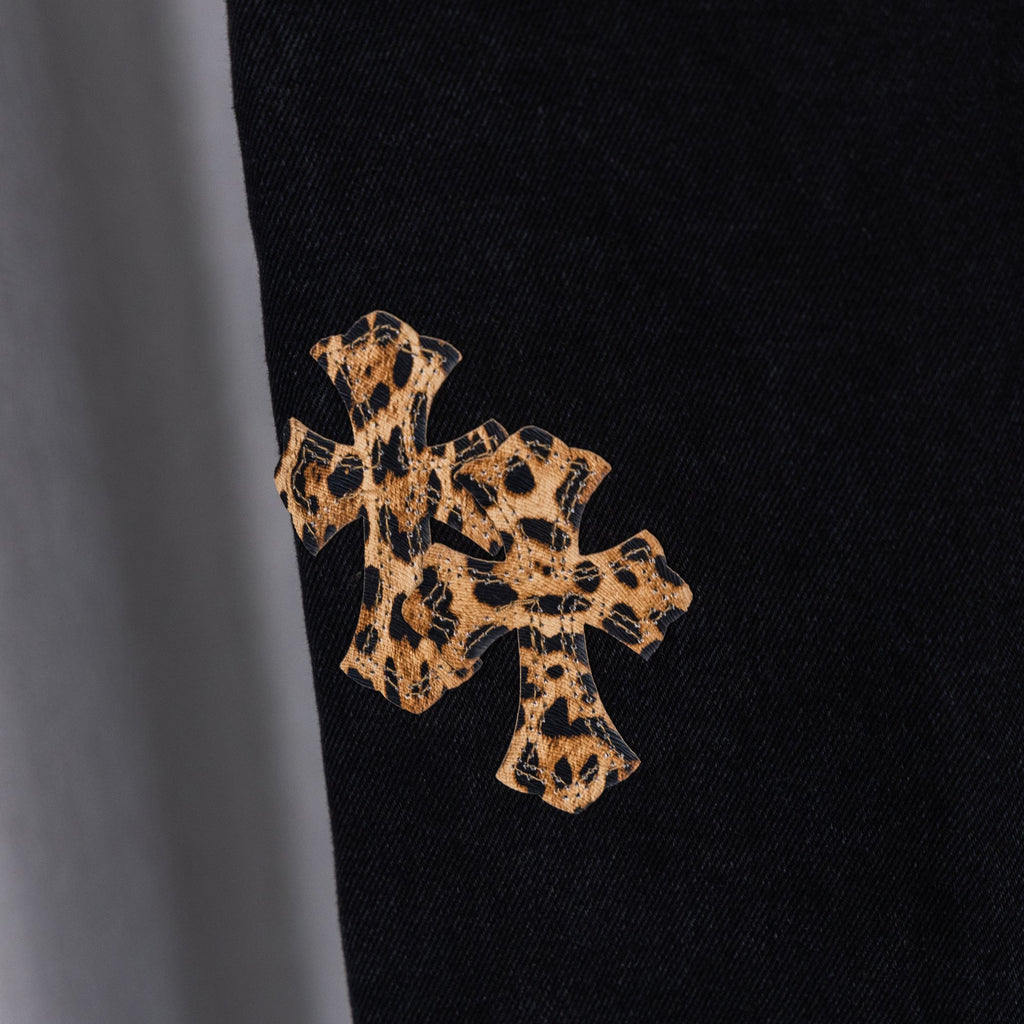 Black denim pants close-up of tan cross embroidery on dark denim