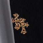 Black denim pants close-up of tan cross embroidery on dark denim
