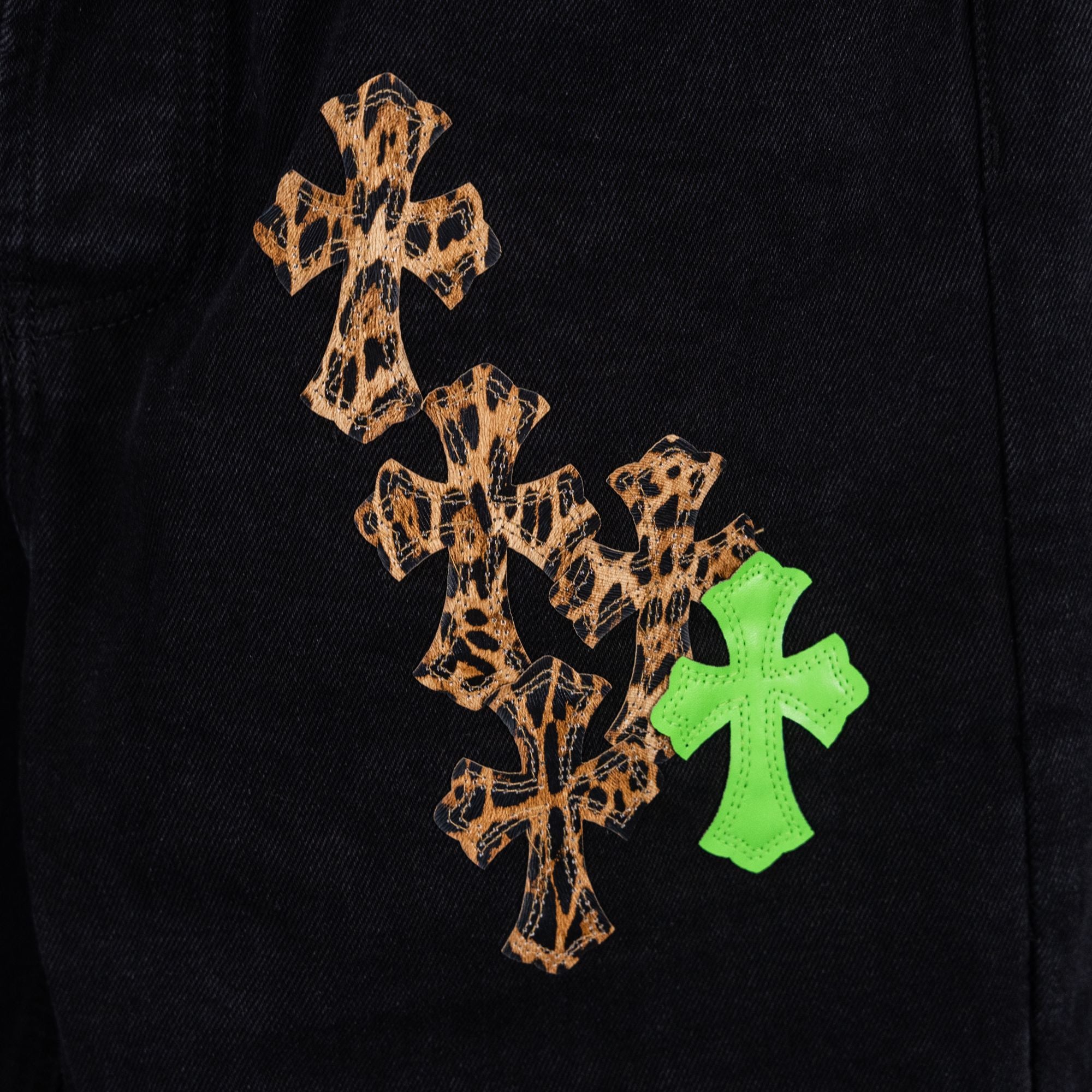 Black denim pants close-up of tan leopard-style cross with green cross accents