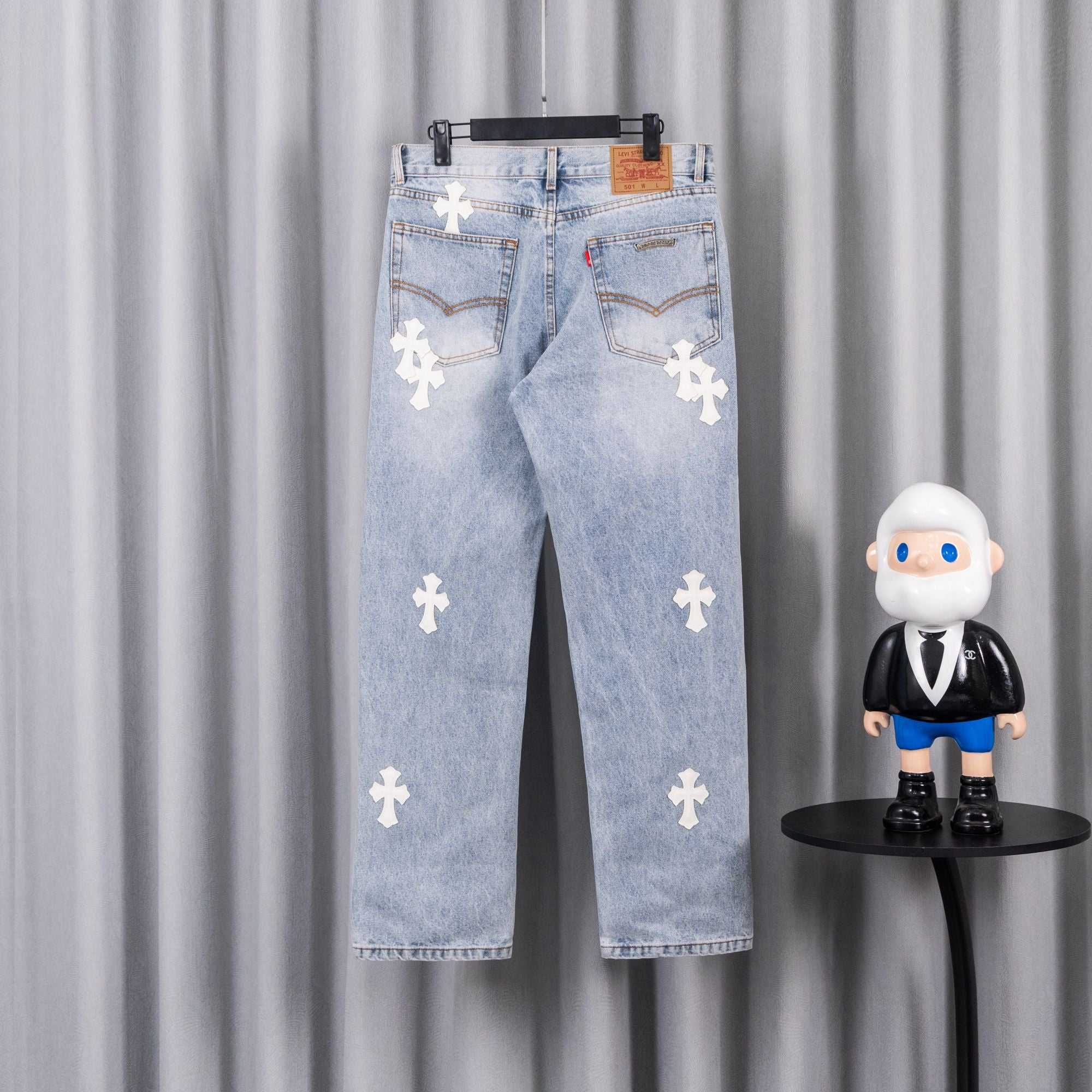 Light blue denim jeans with white cross patches, distressed wash, belt loops.