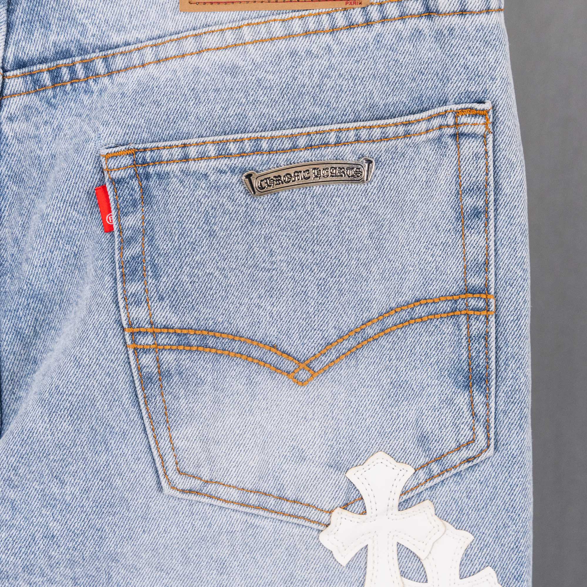 Jeans back pocket with logo tag, curved yoke stitching, and white cross applique.