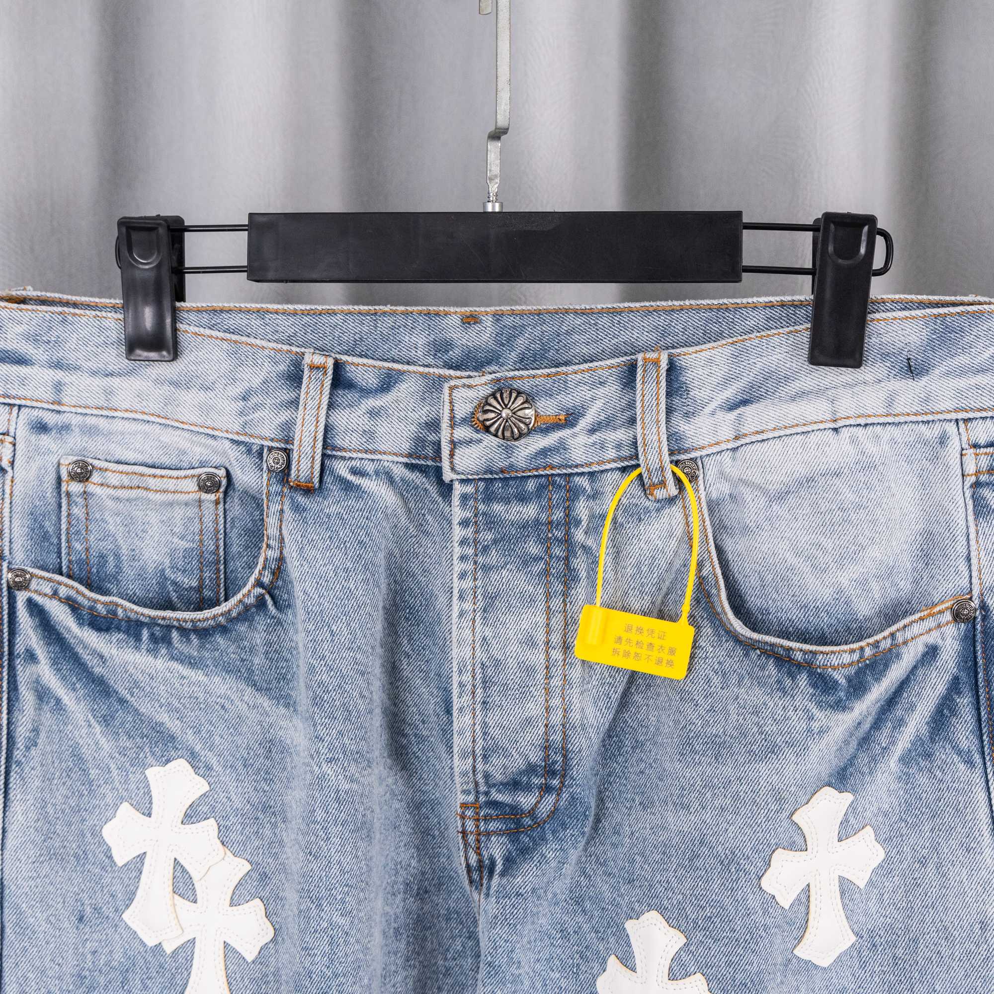 Light blue denim jeans waistband with button, tag, and white cross patches.