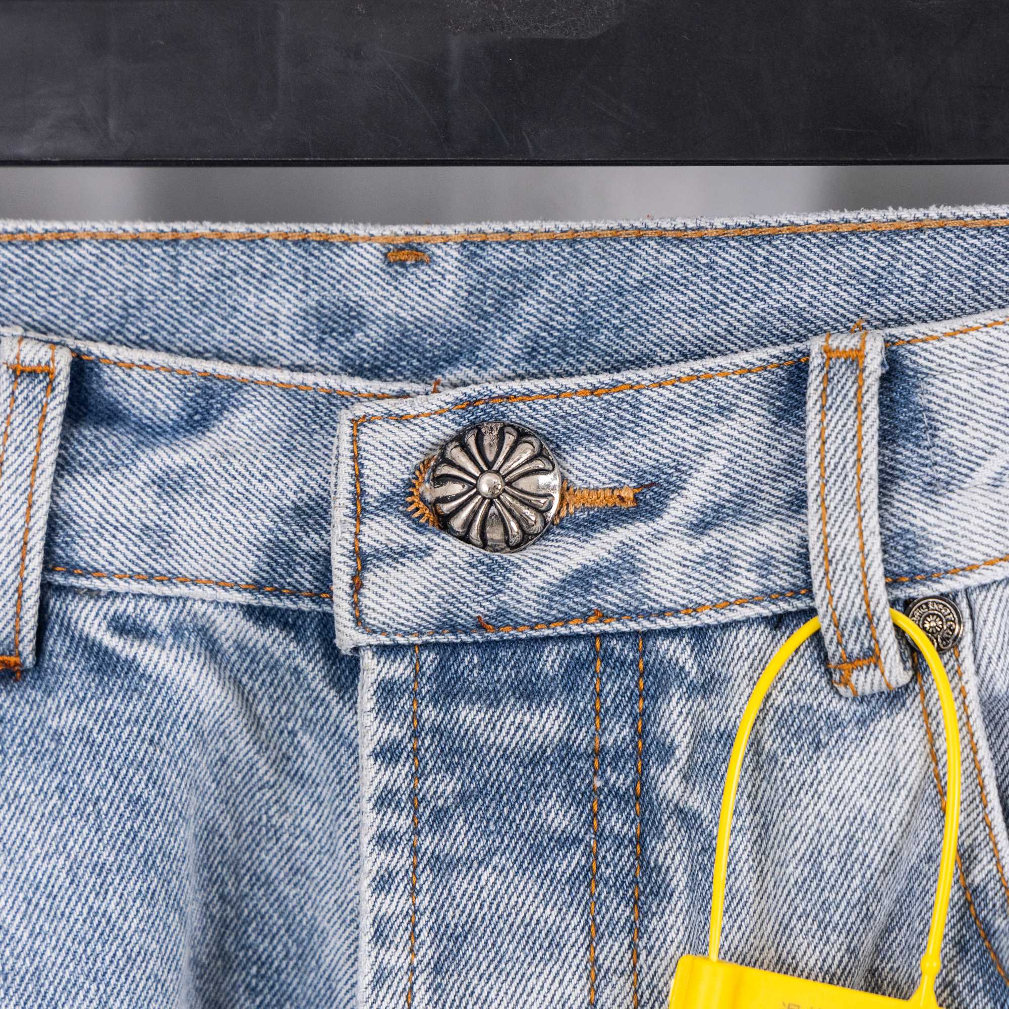 Jeans front pocket detail with white cross embroidery and contrast stitching, close-up.