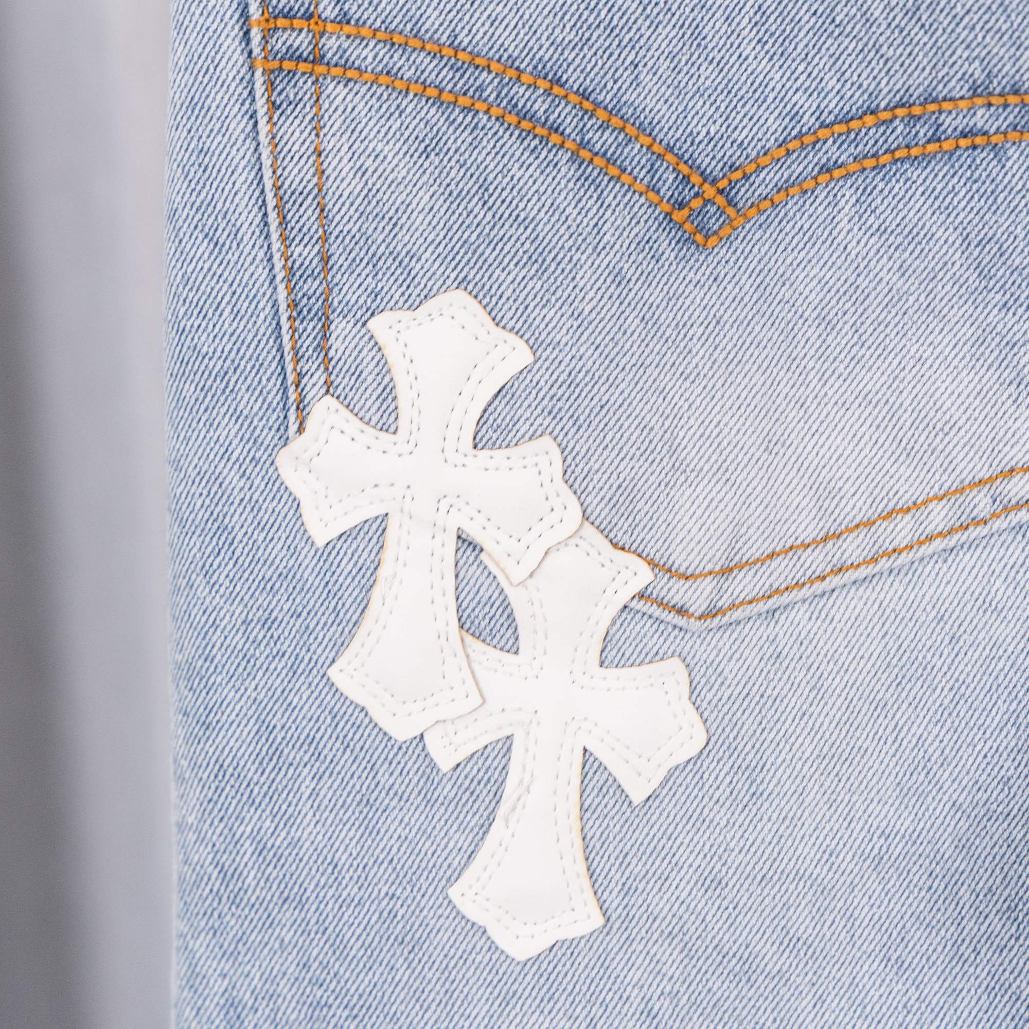 Three white cross patches on light blue denim, close-up of stitched area.