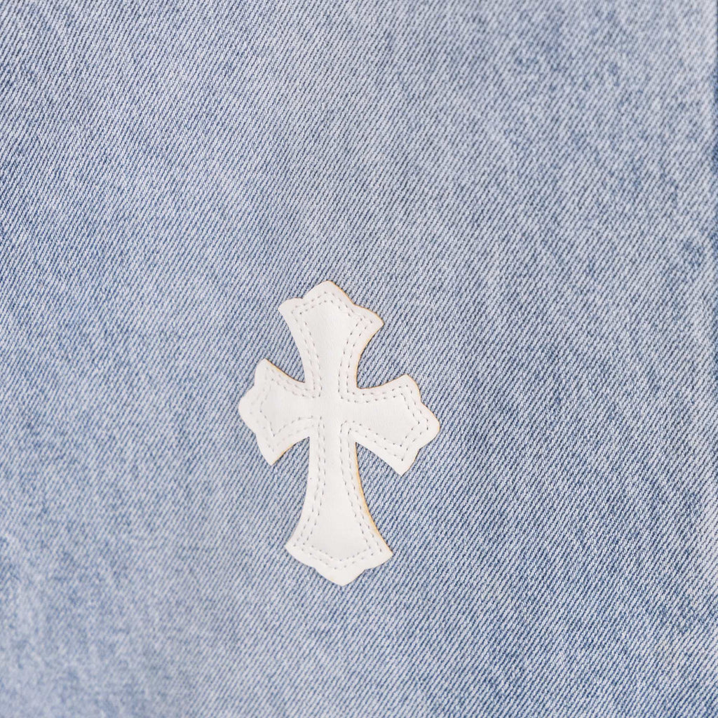 White cross applique on light blue denim, close-up of fabric texture.