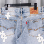 Denim jeans waist and front pockets with white cross patches, button and zip.