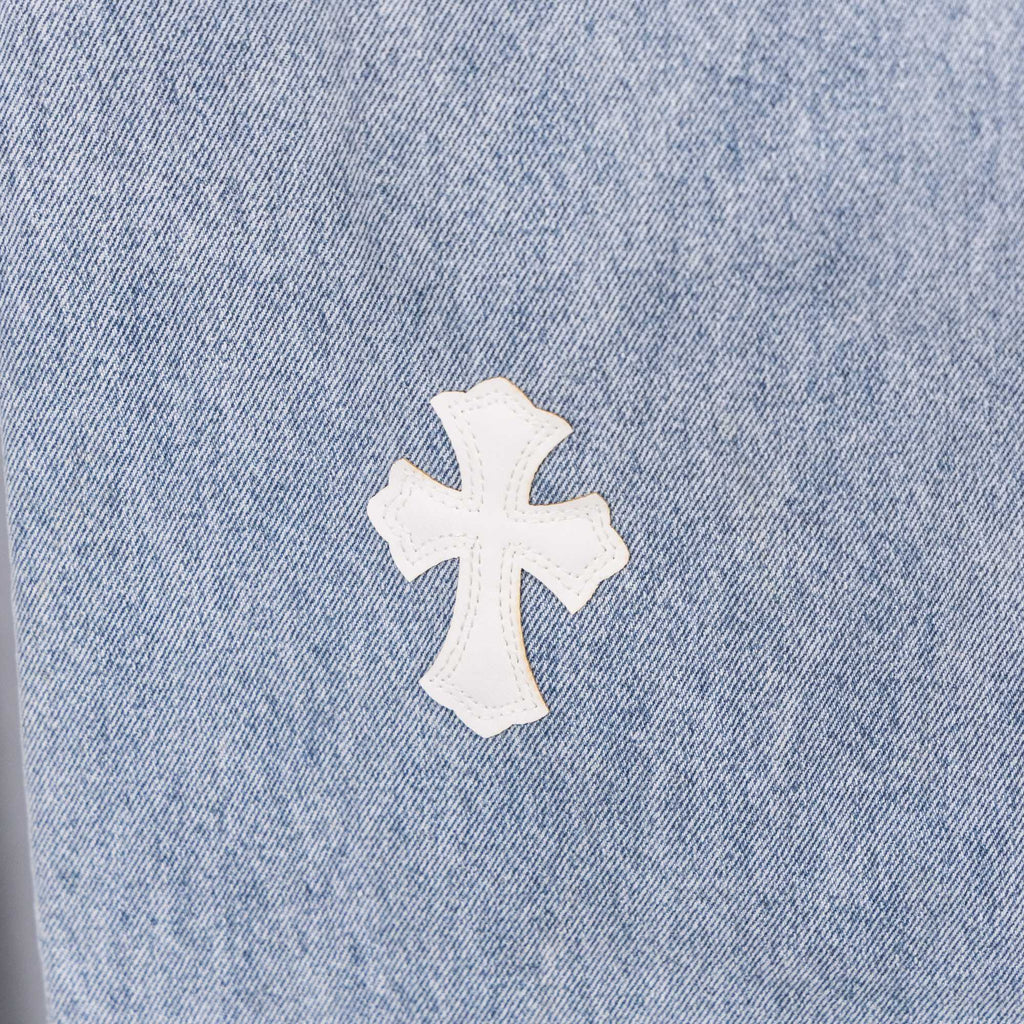 White cross applique on light blue denim, close-up with visible seam texture.
