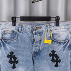 Light blue denim jeans with black cross patches, waistband pockets, and yellow tag