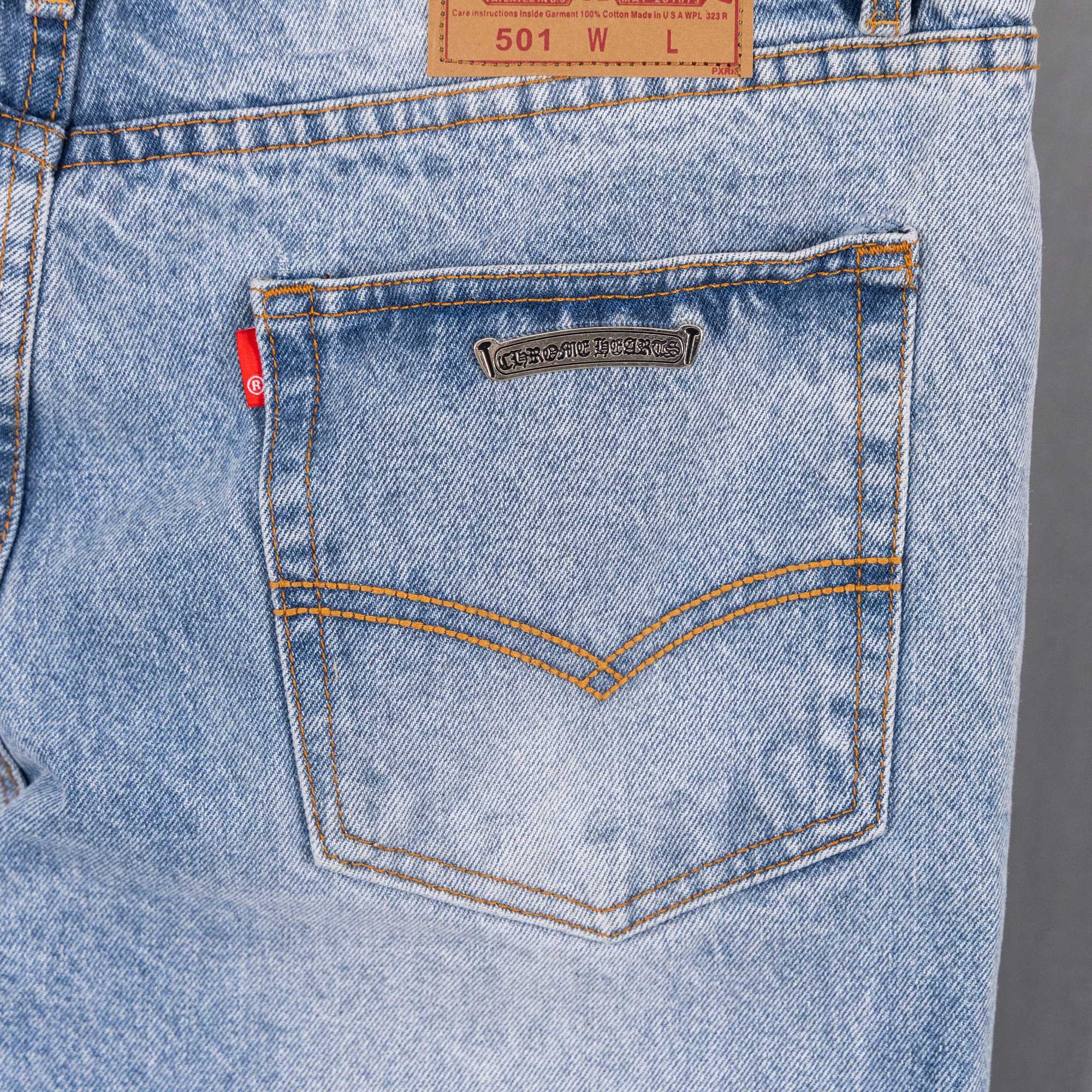 Light blue denim jeans front pocket with bronze label and orange-stitched seams