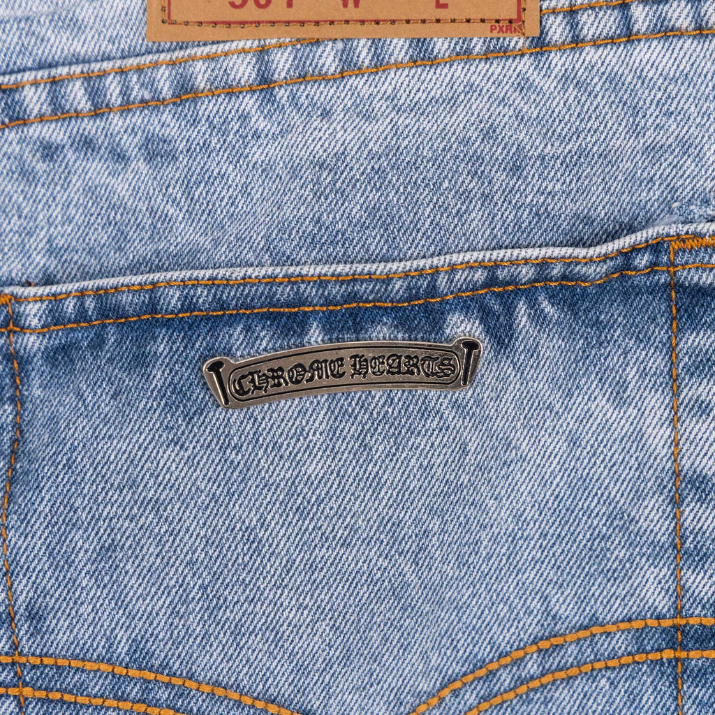 Bronze metal label on light blue denim jeans with orange-stitched seams
