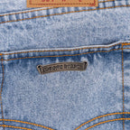 Bronze metal label on light blue denim jeans with orange-stitched seams