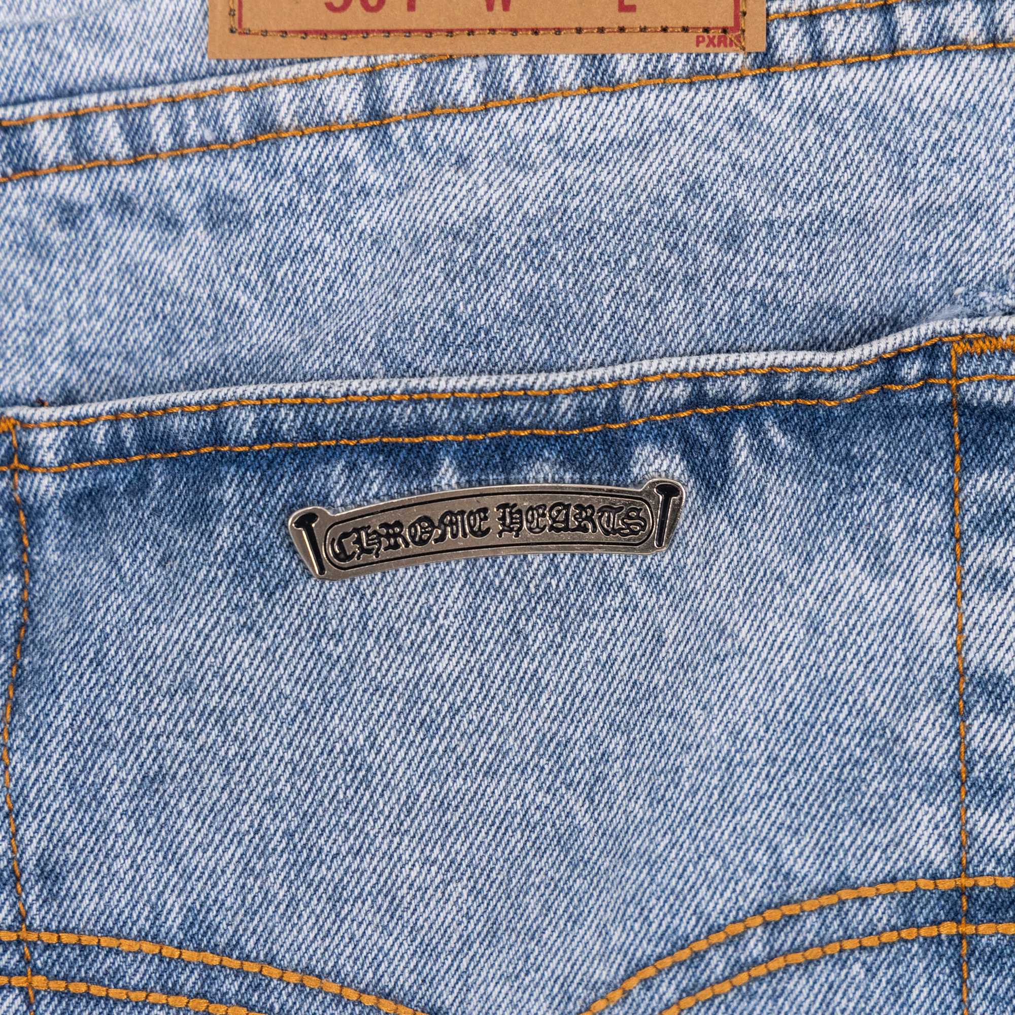 Bronze metal label on light blue denim jeans with orange-stitched seams