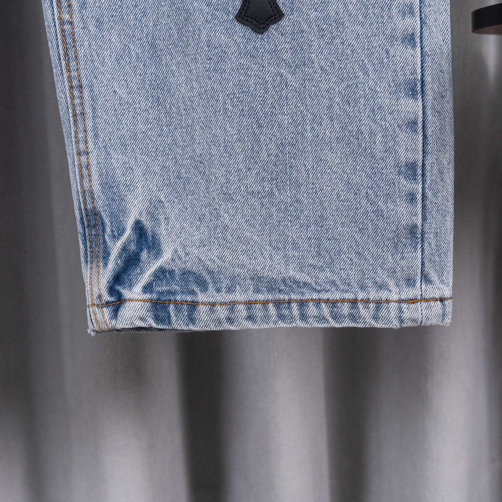 Light blue denim jeans hem with orange-stitched edge and black cross patch