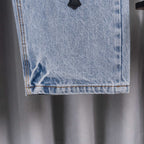 Light blue denim jeans hem with orange-stitched edge and black cross patch