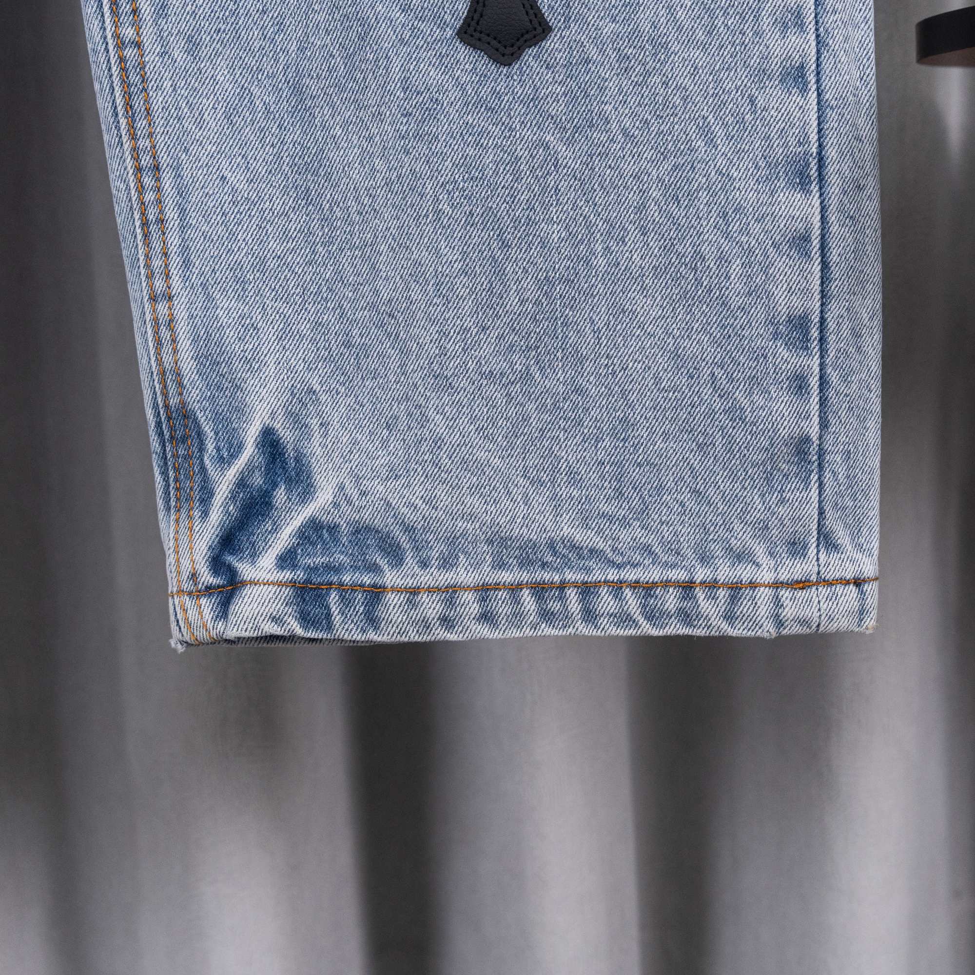 Light blue denim jeans hem with orange-stitched edge and black cross patch