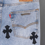Light blue denim jeans front pocket with metal label and black cross patches