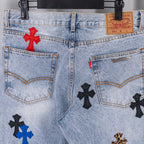 Light blue denim jeans front with button fly, pockets, and cross appliques