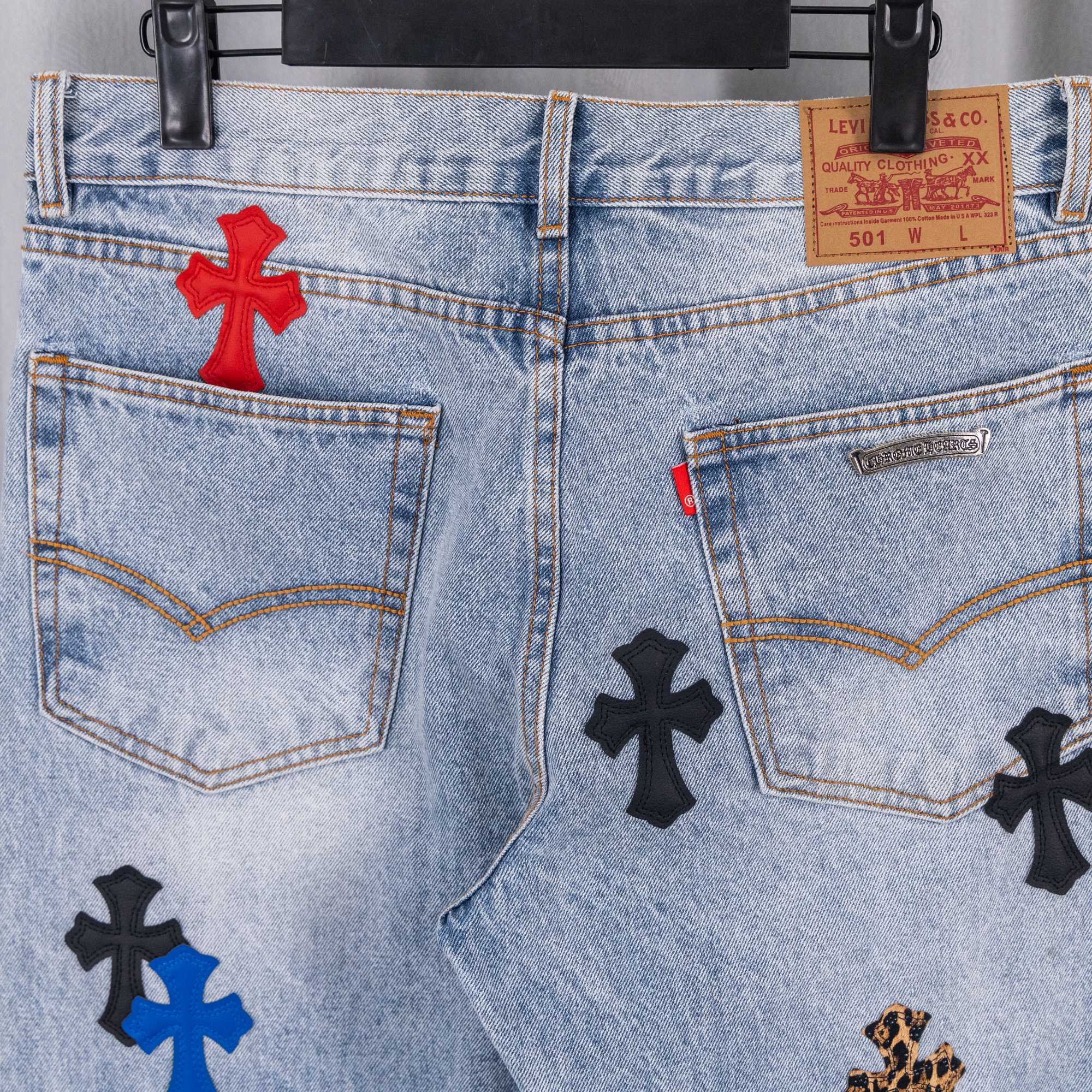 Light blue denim jeans front with button fly, pockets, and cross appliques