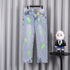 Light blue denim pants with neon green cross patches, front view on hanger