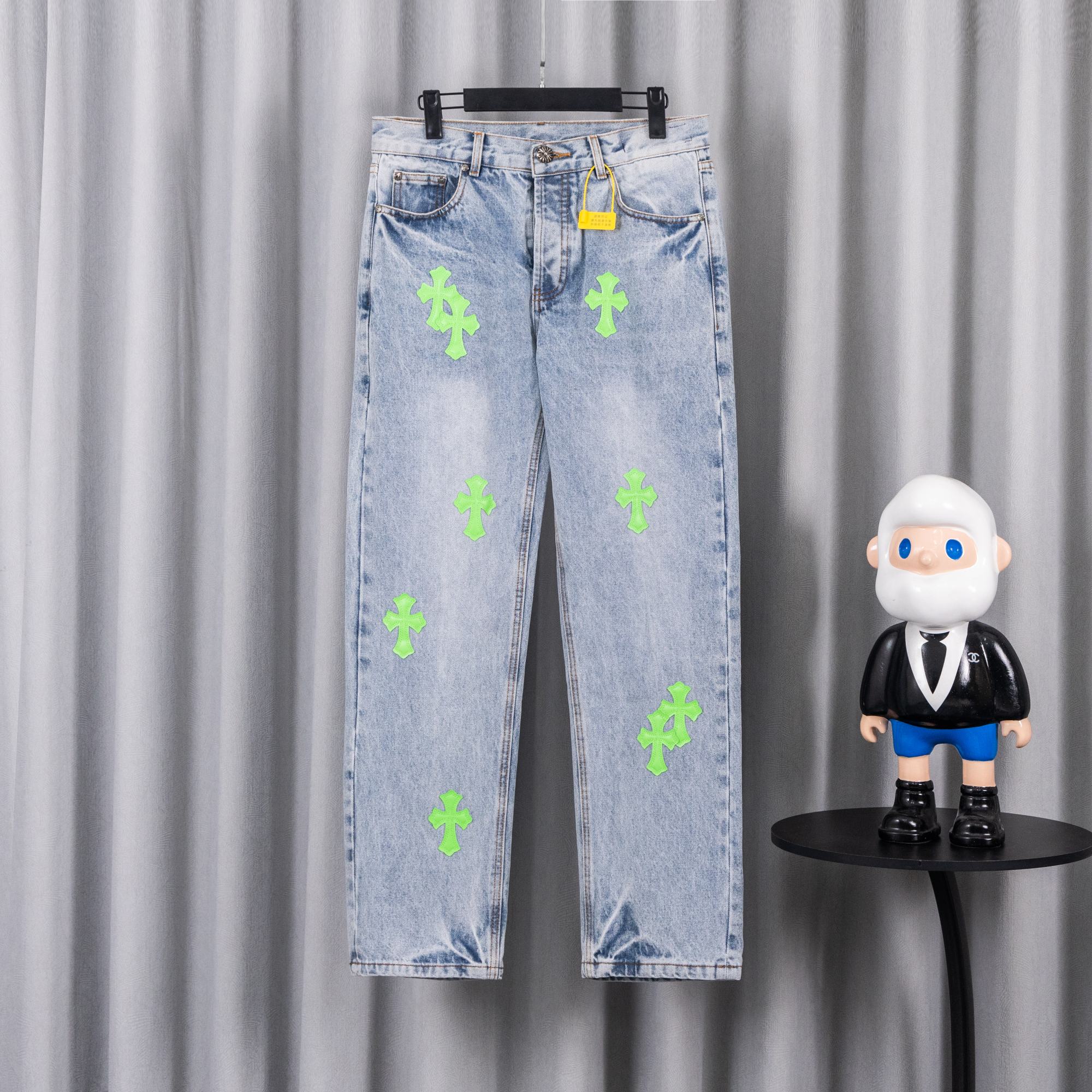 Light blue denim pants with neon green cross patches, front view on hanger