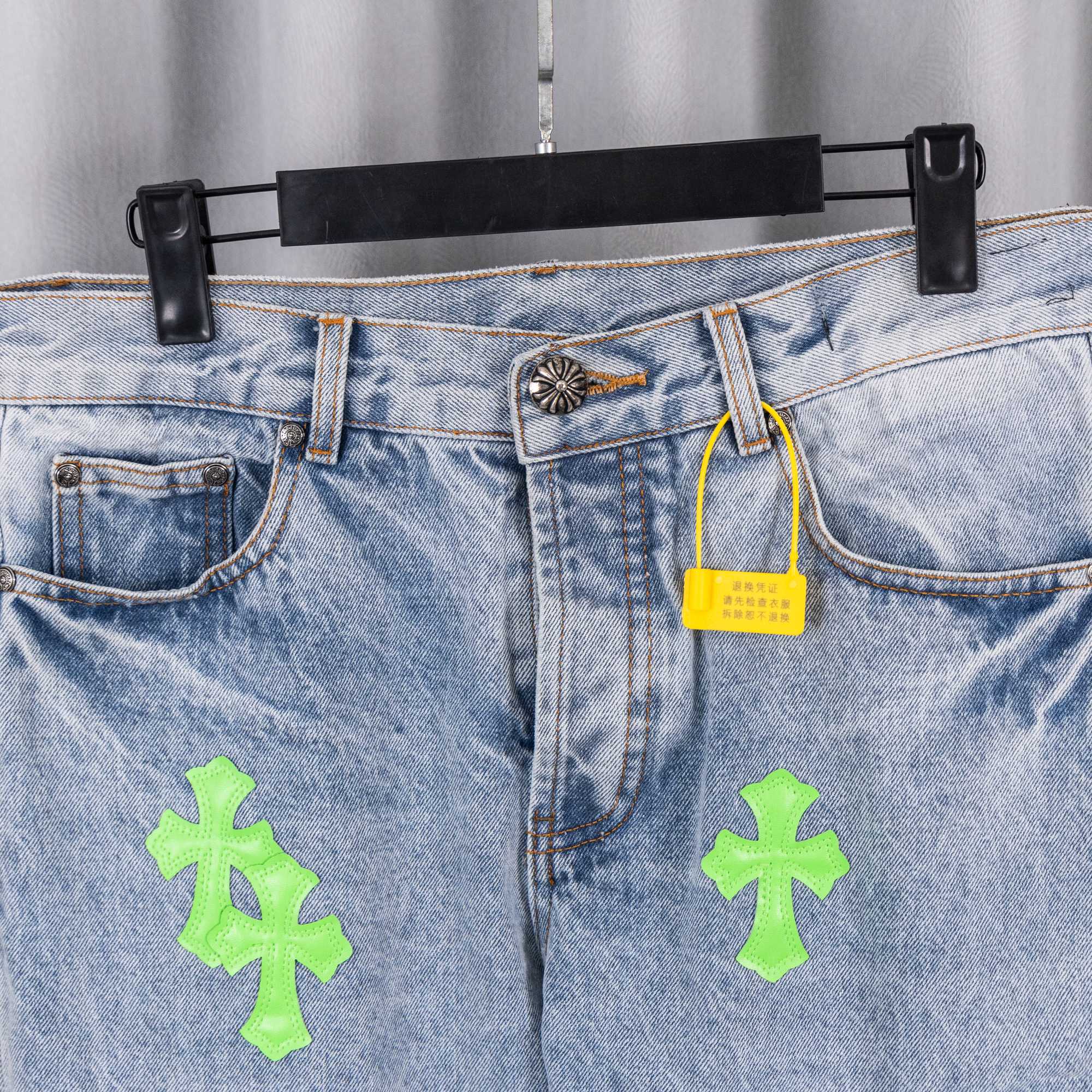 Light blue denim pants close-up of waistband, button fly, and neon green cross patches