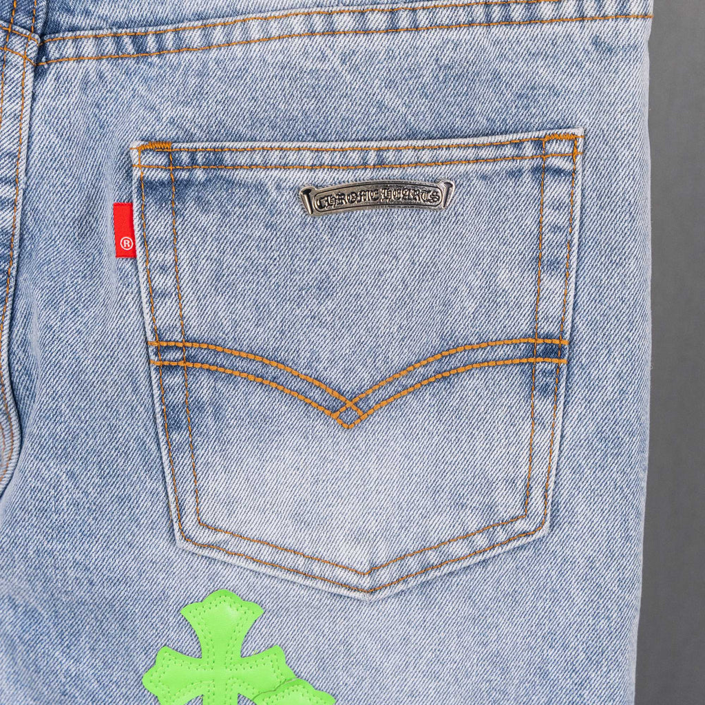Light blue denim pants back pocket close-up with small logo label and neon green cross