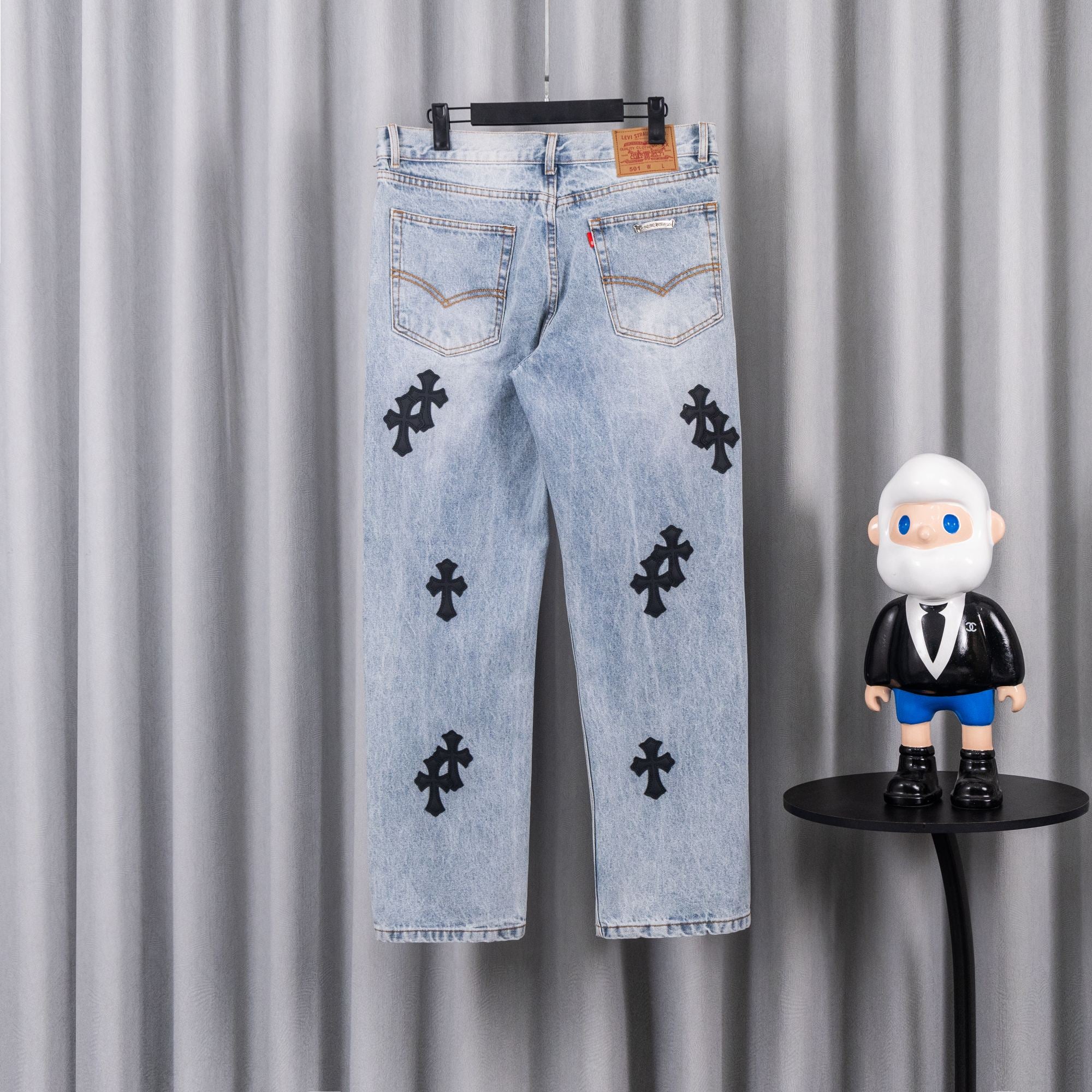 Light wash denim pants with black cross patches and belt loops
