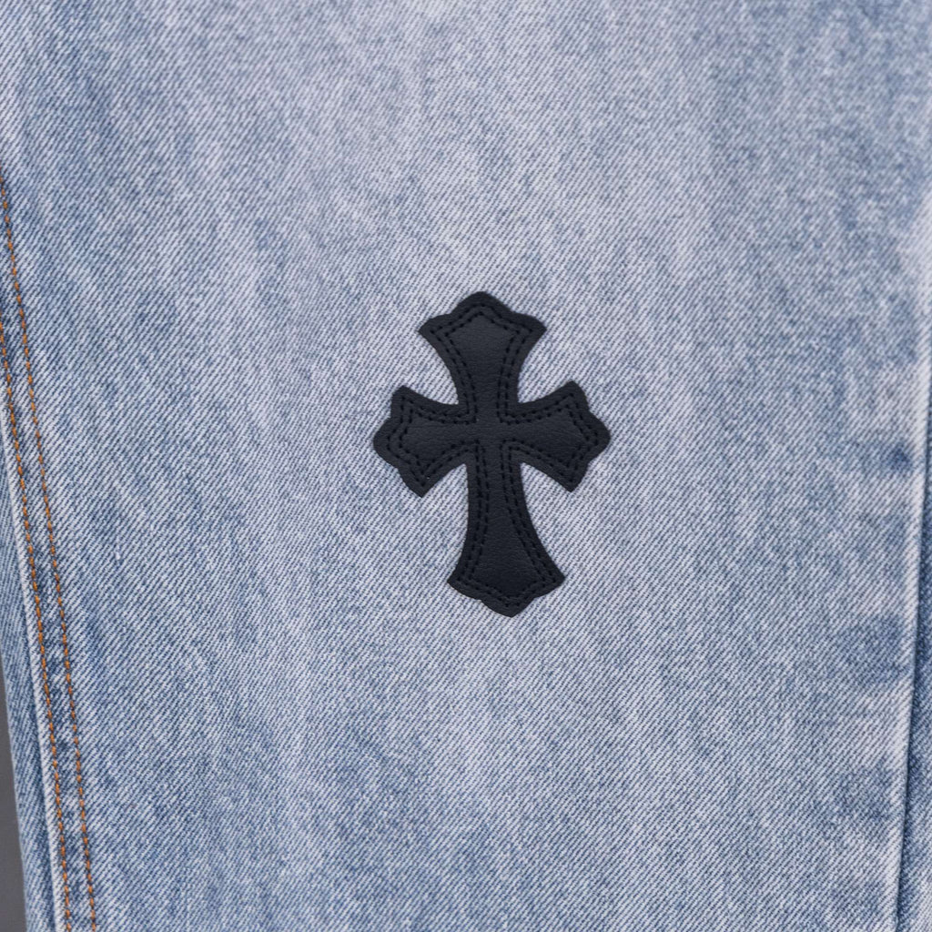 Light wash denim pants with centered black cross patch applique