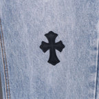 Light wash denim pants with centered black cross patch applique