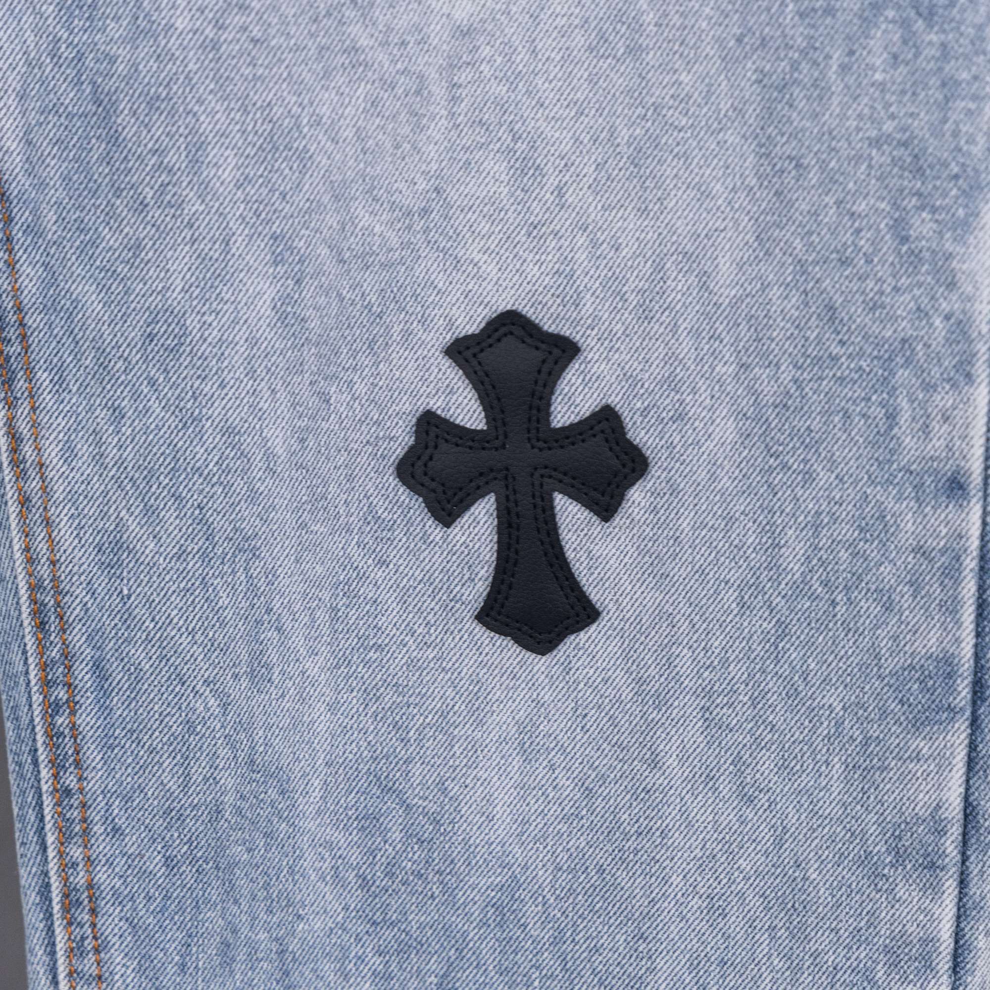 Light wash denim pants with centered black cross patch applique