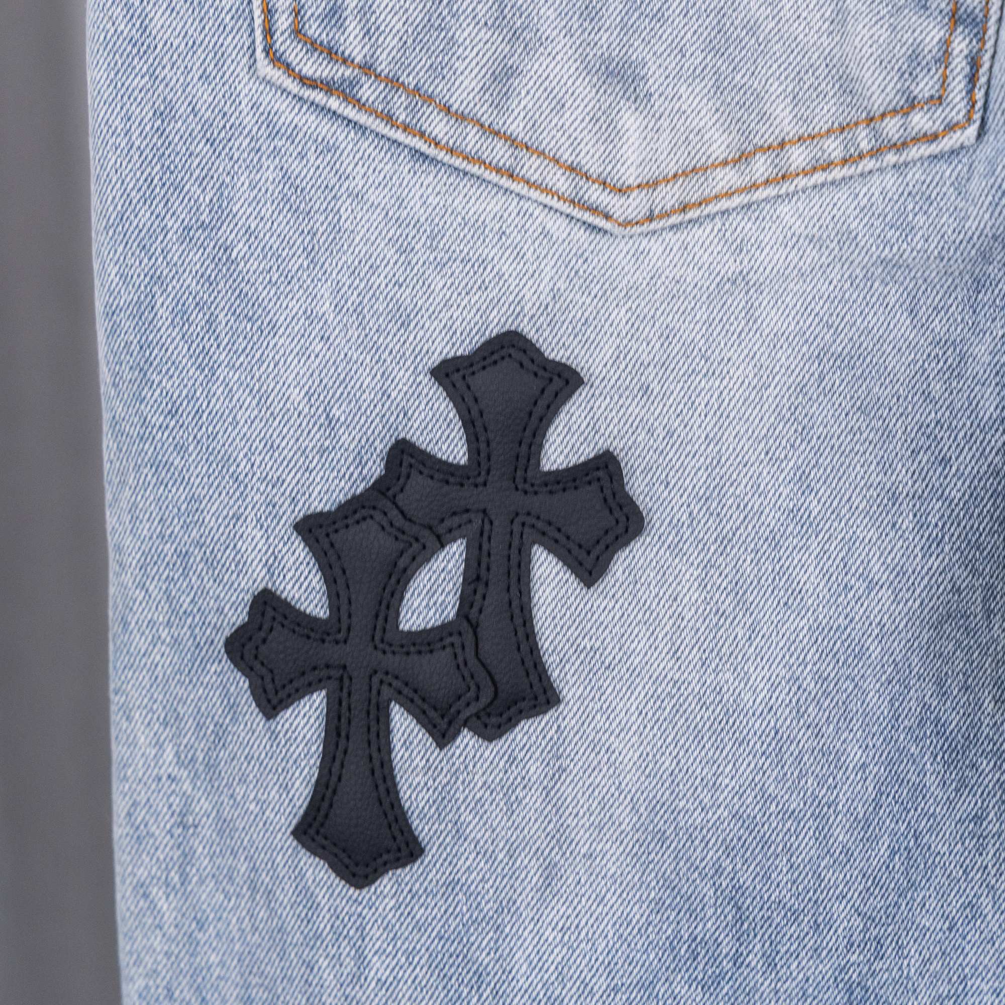 Light wash denim pants with black cross patch applique
