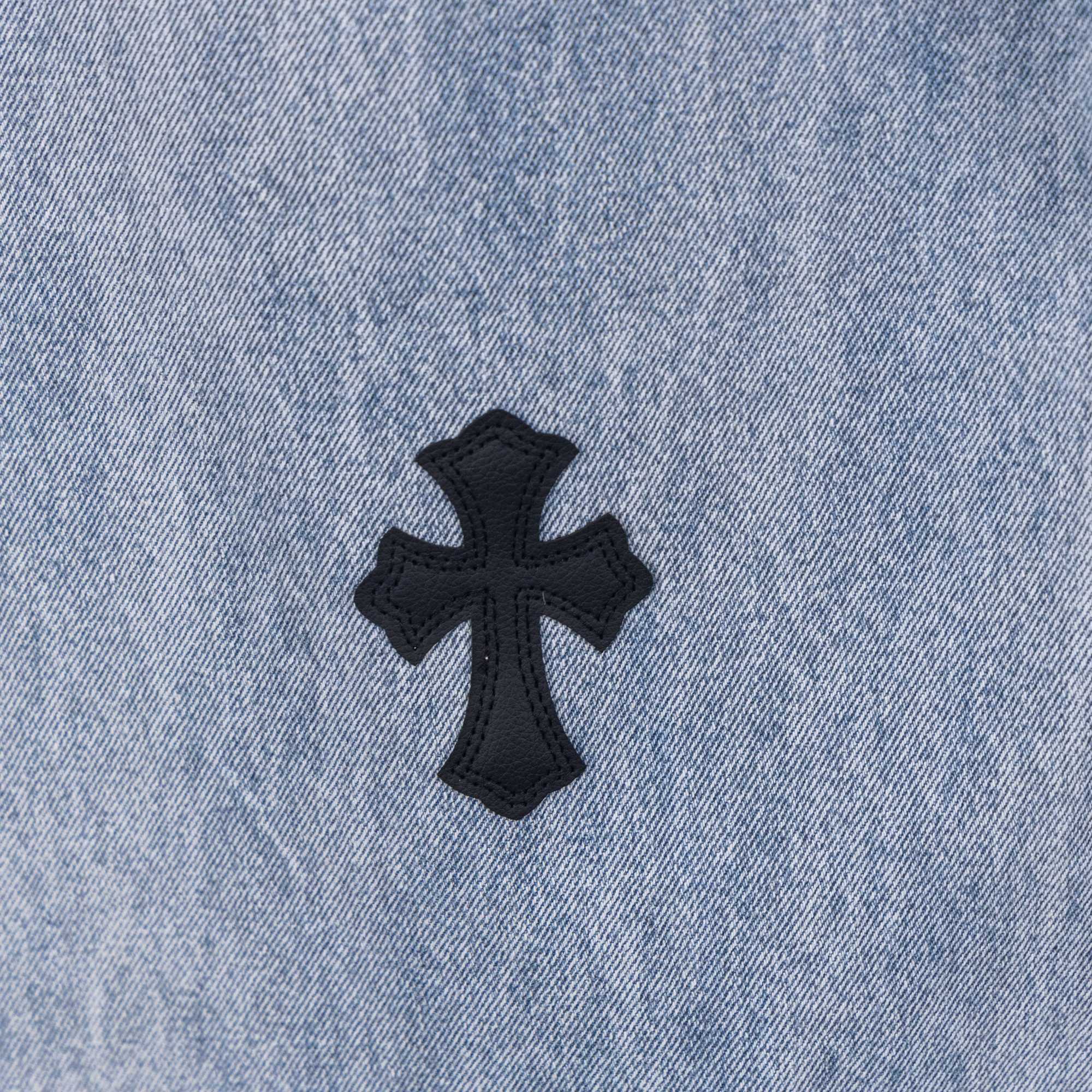 Light wash denim pants with black cross patch applique on fabric