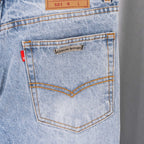 Light blue denim pants back pocket with stitched seams and metal logo patch