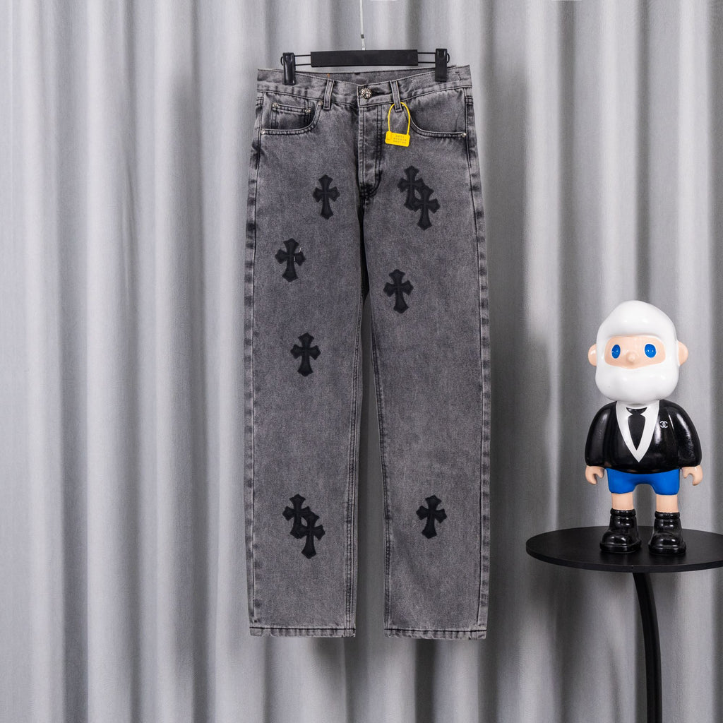 Gray denim pants with black cross applique pattern and button closure, hanging on rack