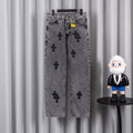 Gray denim pants with black cross applique pattern and button closure, hanging on rack