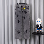 Gray denim pants with black cross applique pattern and button closure, hanging on rack