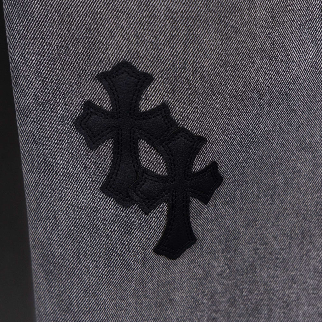 Gray denim pants close-up of large black cross applique