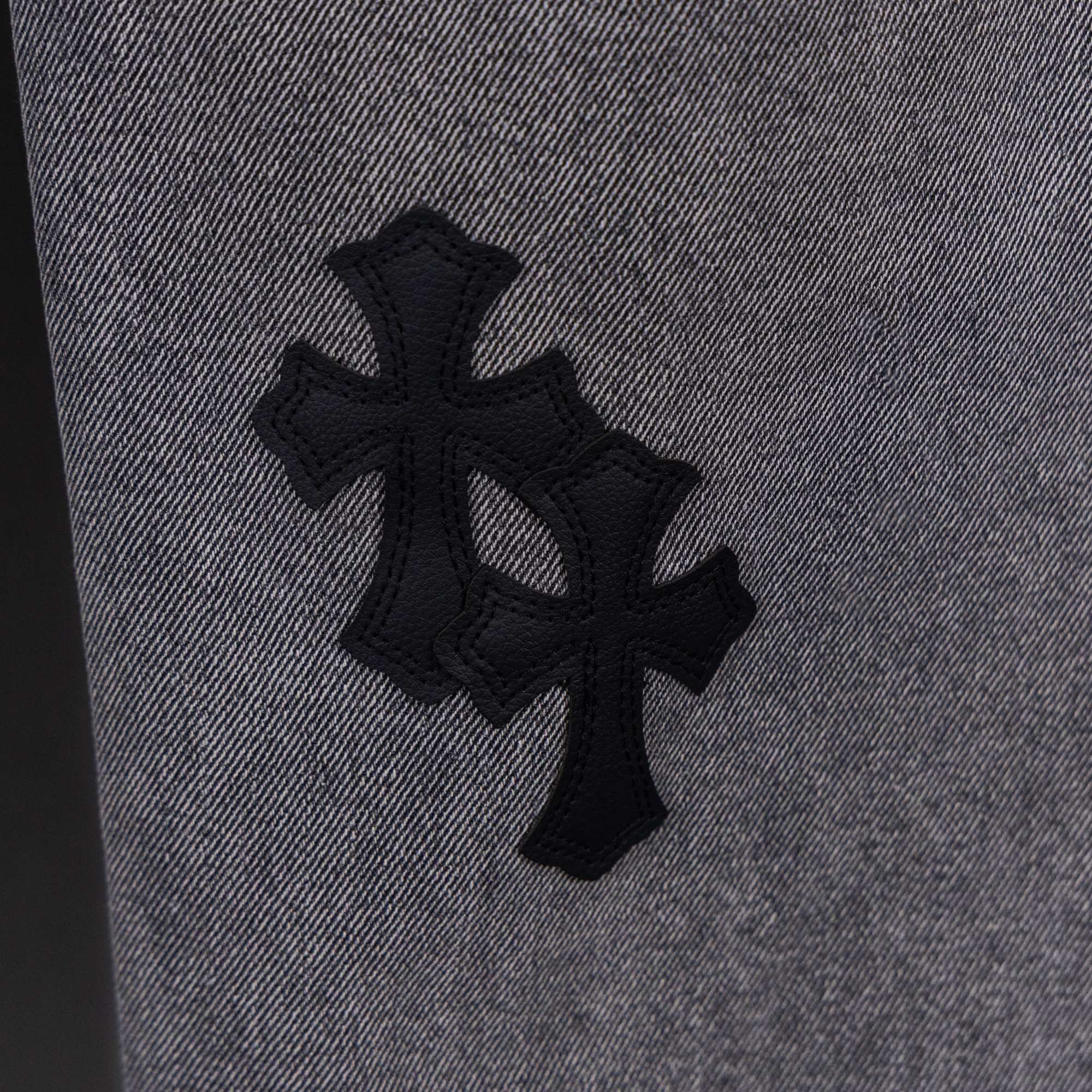 Gray denim pants close-up of large black cross applique