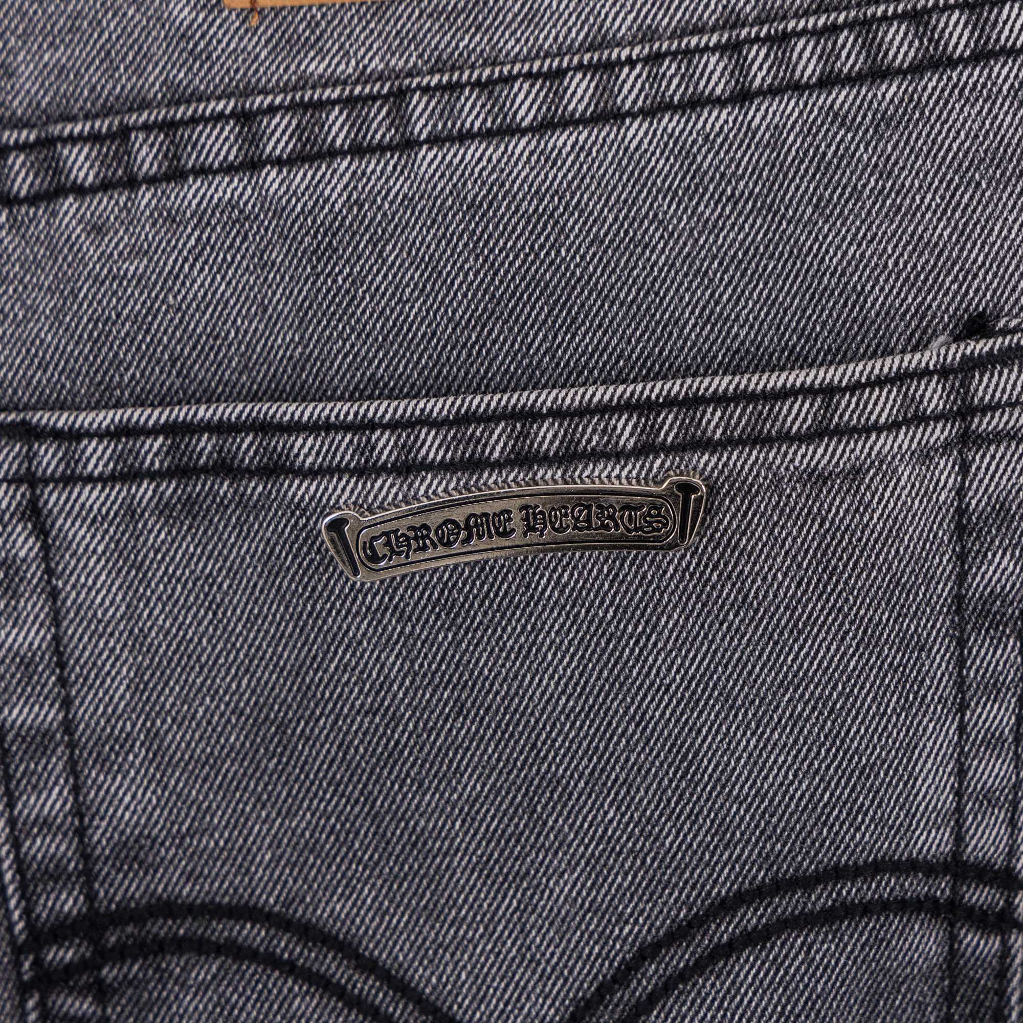 Gray denim pants close-up of back pocket with stitched cross applique